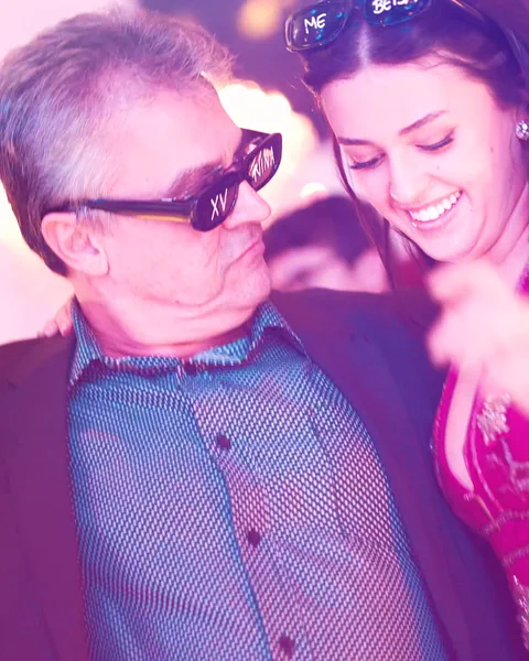 Senhor de óculos de festa dançando com uma moça de rosa, os dois rindo