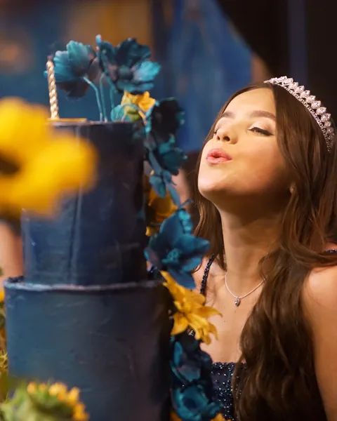 Debutante de tiara soprando a vela do bolo azul com girassóis